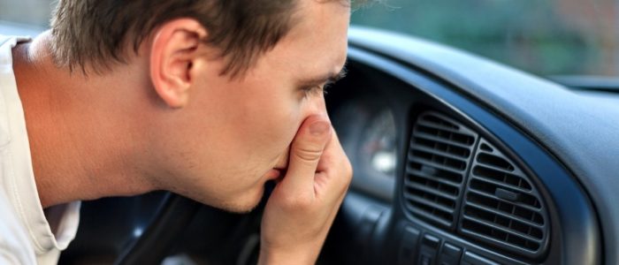 Image depicts a car owner covering their nose because of a bad smell in their car.